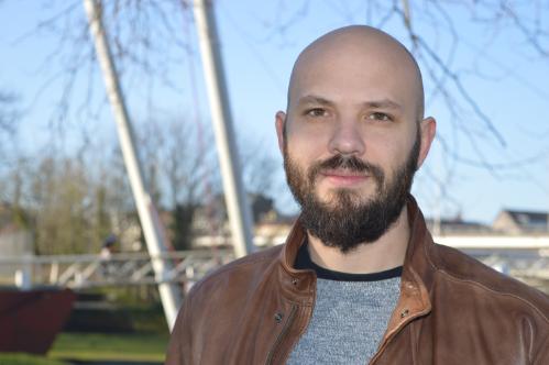 Dr. Osvaldo Bogado Pascottini, a bald man with a beard wearing a brown leather jacket, stands outdoors in front of a blurred background of trees and metal structures